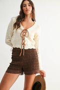 Woman wearing a white lace top and brown shorts with a white background