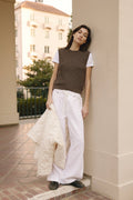 Woman wearing a brown knitted vest and white pants, standing on a sidewalk.