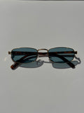 Pair of sunglasses with dark lenses and gold frame on a light gray background