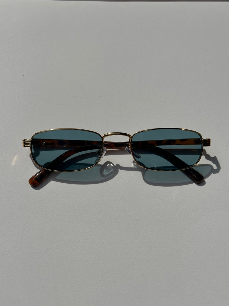 Pair of sunglasses with dark lenses and gold frame on a light gray background