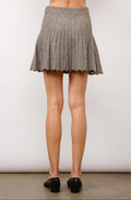 Person wearing a gray pleated skirt with black shoes on a plain background