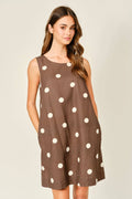 Woman wearing a brown dress with white polka dots on a plain background