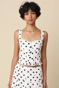 Woman wearing a white sleeveless top with black polka dots against a beige background