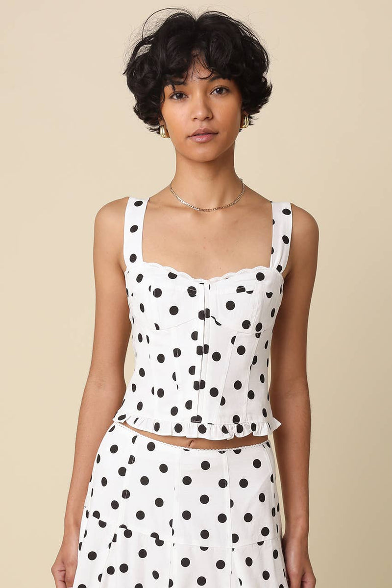 Woman wearing a white sleeveless top with black polka dots against a beige background