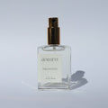 Clear perfume bottle with gold cap labeled 'Genevieve Palo Santo' on a light gray background