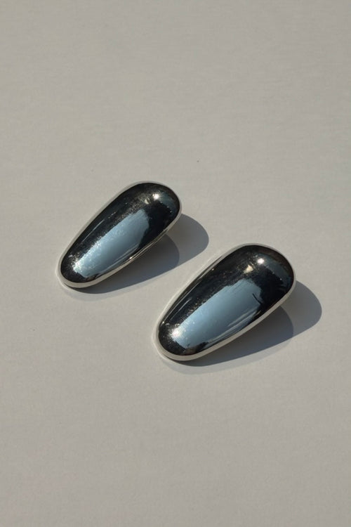 A pair of polished silver-toned oval stud earrings with a highly reflective, mirror-like surface, displayed on a neutral light gray background.