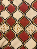 A close-up of a textile or fabric pattern featuring repeating red and cream diamond motifs outlined in black, with tan dotted and zigzag accents.