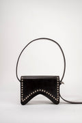 A black leather shoulder bag with a curved, shield-like silhouette, decorated with silver-tone studs along the bottom edge, set against a plain light gray background.
