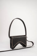 A black leather shoulder bag with a curved top flap, adorned with silver-tone studs along the edges, featuring a single top handle and a long matching shoulder strap on a light gray background.
