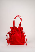 A bright red velvet drawstring bucket bag with long top handles, photographed against a clean, light gray studio background.