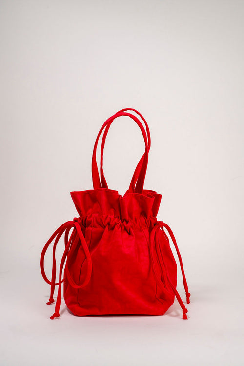 A bright red velvet drawstring bucket bag with long top handles, photographed against a clean, light gray studio background.