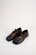 A pair of black leather tabi-style Mary Jane shoes with double straps and buckle details, displayed on a clean white studio background.