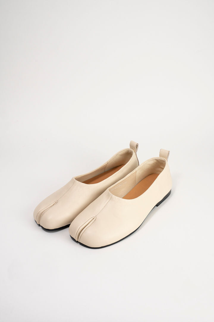 A pair of light beige leather tabi-style flats with a split toe and pull tabs, displayed on a clean white background.
