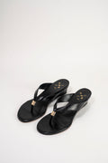 A pair of black leather wedge sandals with gold-tone metal accents on the toe post and insole, displayed on a clean white studio background.