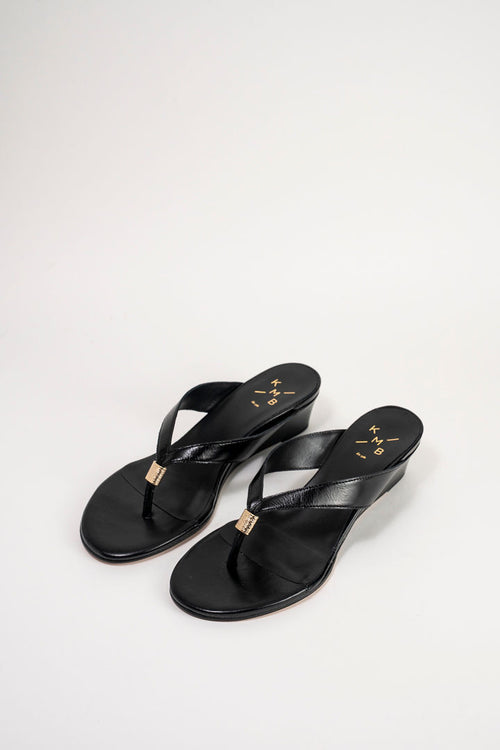A pair of black leather wedge sandals with gold-tone metal accents on the toe post and insole, displayed on a clean white studio background.