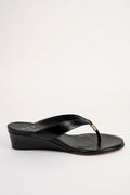 A single black leather wedge thong sandal with a small gold-tone metal accent on the strap, shown from a side profile against a plain white background.