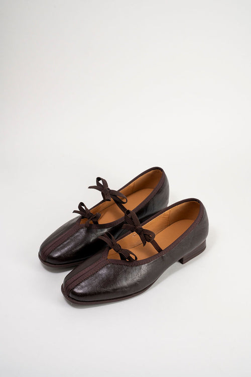 A pair of dark brown leather Mary Jane flats with matching lace-up straps, displayed on a clean white background.