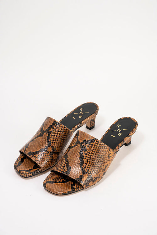 A pair of women's heeled mule sandals featuring a brown and black snakeskin pattern, displayed on a clean white background.