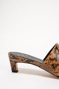 A close-up side view of a heeled mule sandal featuring a brown and black snakeskin pattern, set against a plain white background.