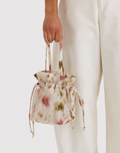 Floral-patterned handbag held by a person wearing white pants on a light background