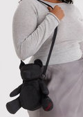 Person holding a black teddy bear-shaped bag against a white background