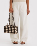 Person holding a checkered bag wearing white pants on a plain background