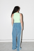 A model is shown from behind wearing a light mint green sleeveless top and wide-leg blue corduroy pants with a white side stripe, standing against a plain white wall.