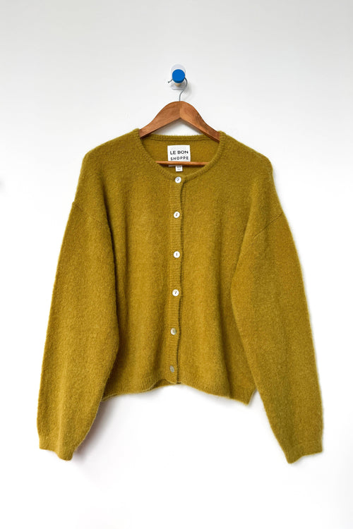 Mustard yellow cardigan on a wooden hanger against a white background