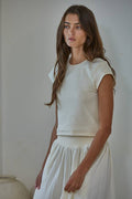 Woman wearing a white top and skirt against a plain background