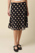 Person wearing a black polka dot skirt on a beige background