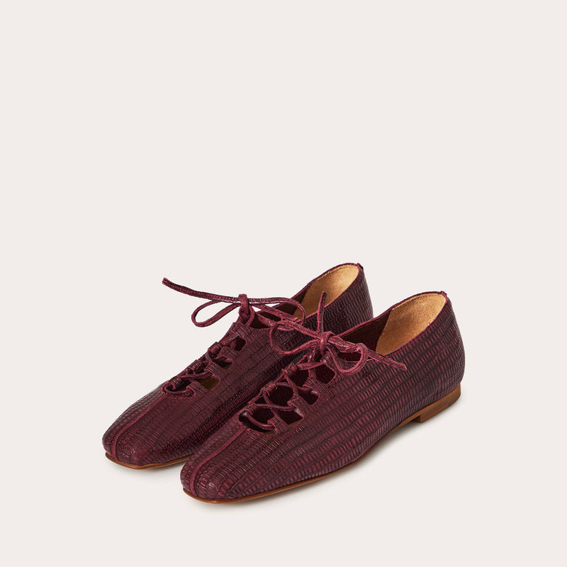 Pair of maroon shoes with lace-up design on a light gray background