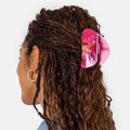 Person with braided hair wearing a pink hair clip on a white background