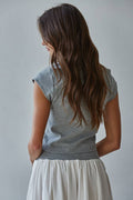 Woman wearing a gray sleeveless top and white skirt against a plain background