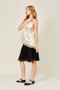 Woman wearing a white satin top and black lace skirt on a plain background