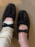 Black flats with bow details worn indoors on a textured surface
