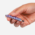 A hand holding a small, cylindrical novelty item with a purple, lavender, and white scale-like pattern and black ends, shown against a plain light gray background.