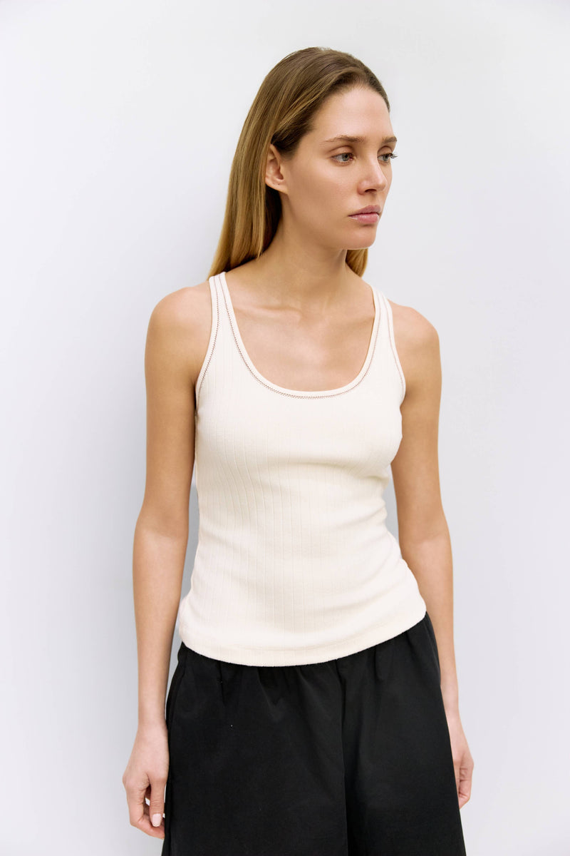 Woman wearing a white tank top and black pants against a light gray background