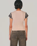 A model shown from the back wearing a light peach sleeveless top with black and white plaid short sleeves, paired with dark gray jeans, against a solid light gray background.