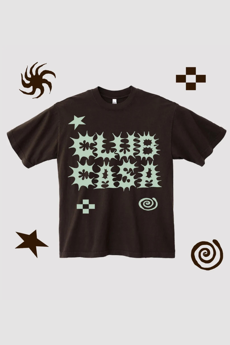 A dark brown short-sleeve t-shirt with a light green abstract graphic print on the front, displayed against a light gray background with decorative brown doodle elements in the corners.