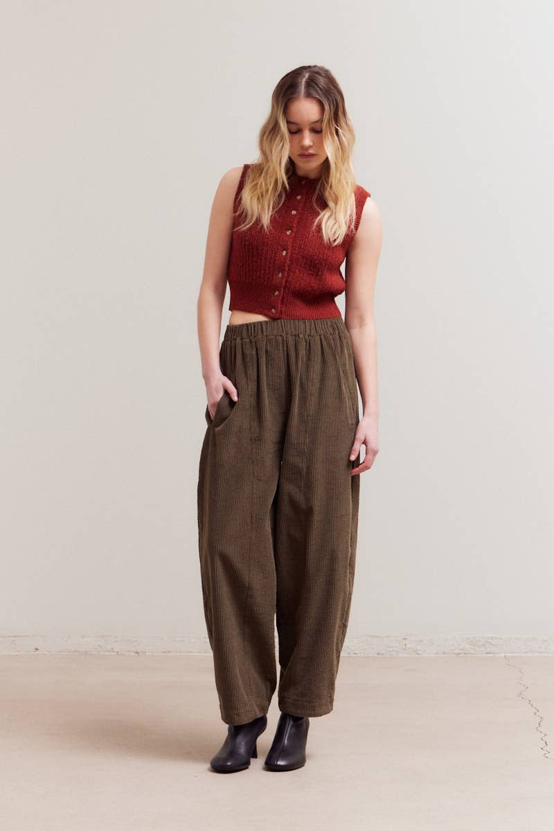 Woman wearing a red sleeveless top and brown high-waisted pants against a plain background