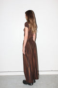 Woman wearing a brown textured dress standing against a white wall.