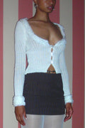 Person wearing a white ribbed sweater over a black pinstripe skirt against a striped wall.
