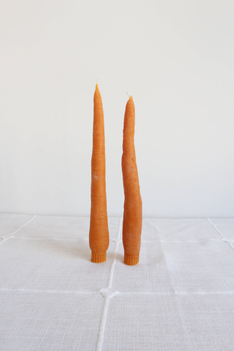 Two orange candles on a white tiled surface