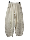 A pair of loose, wide-leg linen pants in a light beige color, hanging from black plastic clips against a plain white background.