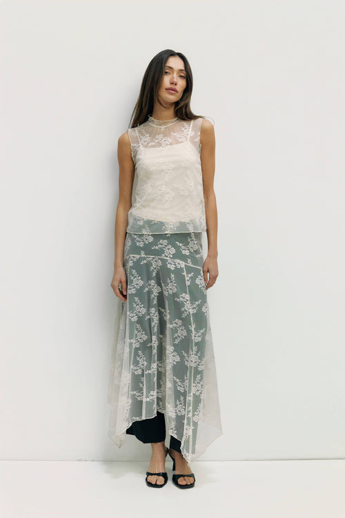 Woman wearing a sleeveless lace top and floral skirt on a white background