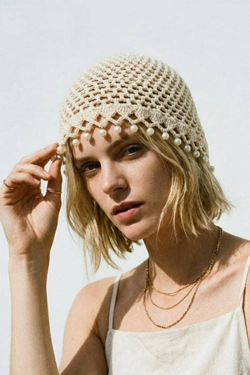 Woman wearing a beige crochet hat with pearl embellishments against a light background