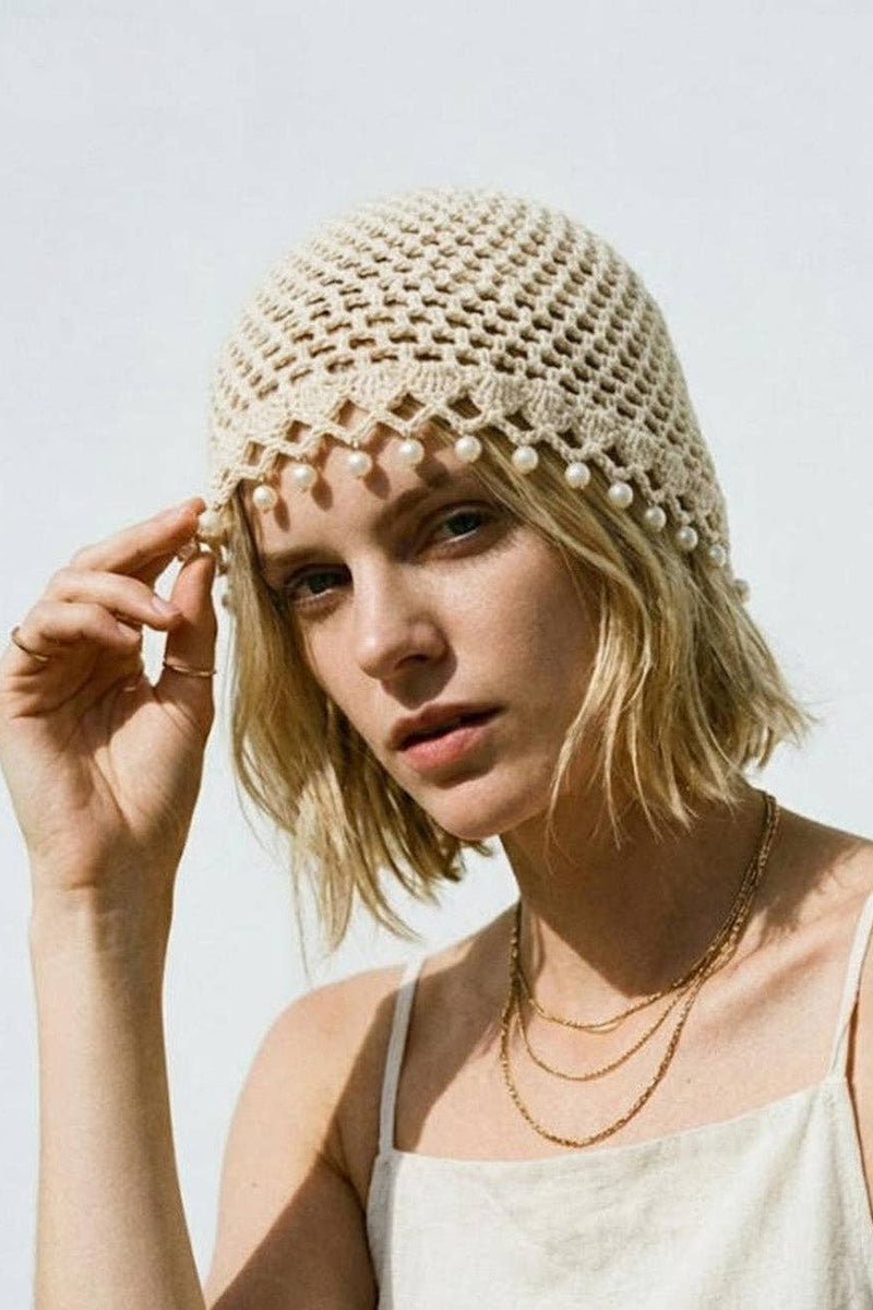 Woman wearing a beige crochet hat with pearl embellishments against a light background