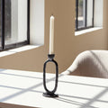 Black candle holder with a white candle on a light surface, with a blurred background