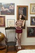 Woman in a red and white outfit standing in a room with vintage paintings on the wall.