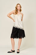 Woman wearing a white lace top and black shorts on a plain background